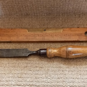 May include: A wooden level with a brass inlay and a wooden chisel with a metal blade. The level has markings for inches and the chisel has the word "Stanley" engraved on the blade.