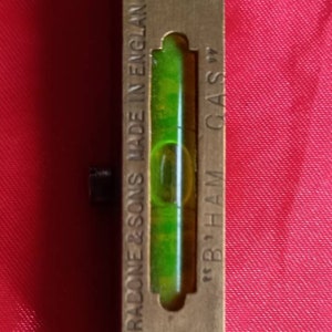 May include: Vintage brass level with a green vial, marked "J. RADONE & SONS MADE IN ENGLAND" and "B' HAM GAS". The level has a rectangular shape with rounded ends and is secured with two screws.