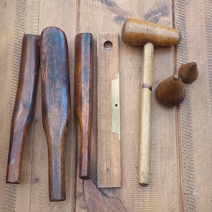 Peut inclure: Ensemble d'outils de menuiserie anciens, comprenant des maillets en bois, une règle avec des détails en laiton et diverses pièces en bois de formes variées. Les outils sont disposés sur une surface en bois, mettant en valeur leur aspect vieilli et leur savoir-faire.