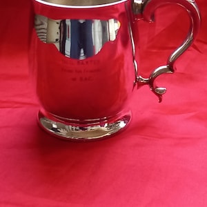 May include: A silver tankard with a handle shaped like a bird's head. The tankard is engraved with the text "Bill Baxter from his/friends at BAC."