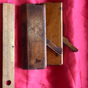 May include: A vintage wooden hand plane with a brass level on the side. The plane is closed and has a dark brown finish.