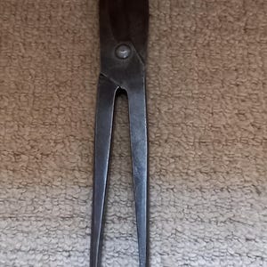 May include: A pair of vintage metal shears with a pointed tip and a rounded handle. The shears are made of dark metal and have a worn, rustic look.