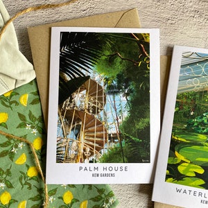 Peut inclure: Une carte postale repr&eacute;sentant une peinture de la Palm House des Jardins de Kew. L'image montre un escalier en colima&ccedil;on &agrave; l'int&eacute;rieur de la structure en verre avec une v&eacute;g&eacute;tation luxuriante verte qui l'entoure. Le texte "PALM HOUSE" et "KEW GARDENS" est imprim&eacute; sous l'image.