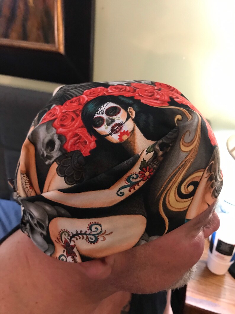 May include: A black and red bandana with a skull and floral design. The bandana features a woman with a sugar skull makeup design.