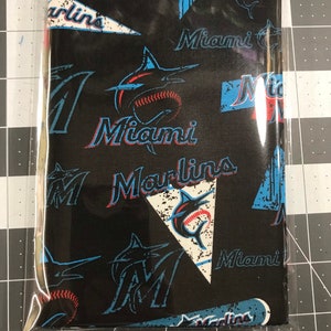 May include: Black fabric with a repeating pattern of the Miami Marlins logo. The logo features a blue marlin fish, a baseball, and the words "Miami Marlins".