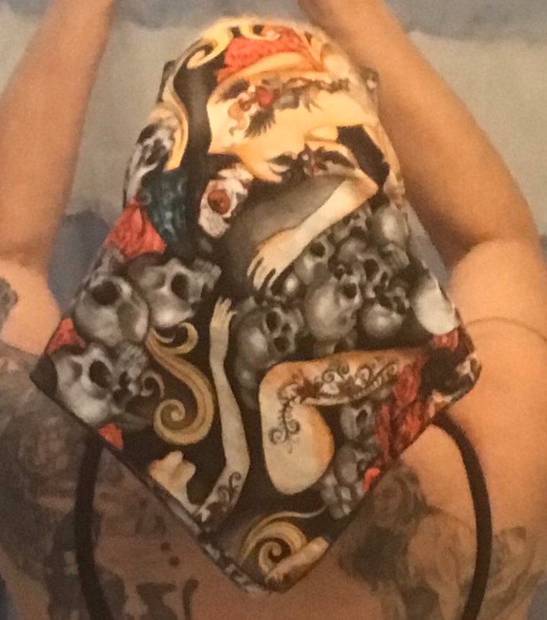 May include: A black fabric head wrap with a skull and crossbones pattern. The fabric features a white and gold design with a red rose and a woman's arm.