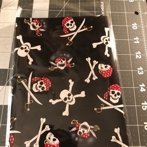 May include: Black fabric with a repeating pattern of white pirate skulls and crossbones with red bandanas.
