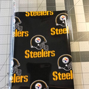 May include: Black fabric with a repeating pattern of yellow Steelers logos and helmets. The fabric is packaged in a clear plastic bag.