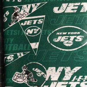 May include: Green fabric with a repeating pattern of white New York Jets logos, helmets, and text. The design includes the team name, the letters "NY", and footballs. The fabric has a distressed, vintage look.
