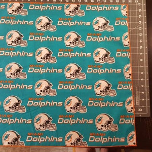 May include: Teal fabric with a repeating pattern of white Miami Dolphins helmets and the words "Miami Dolphins".