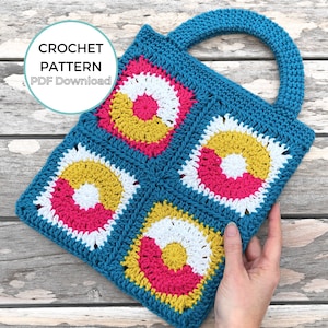 Op de afbeelding: Een gehaakte tote bag met een turquoise blauwe basis en kleurrijke ronde ontwerpen in roze, geel en wit. De tas heeft een handvat en de tekst "CROCHET PATTERN PDF Download" is zichtbaar in een cirkel.