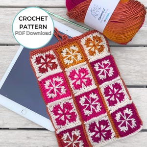 May include: A colorful, crocheted tablet sleeve featuring a floral pattern in shades of pink, orange, and cream. The sleeve is made of square motifs and has a matching border. The image also includes a ball of yarn, a crochet hook, and the text "CROCHET PATTERN PDF Download."