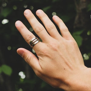 May include: A silver ring with three bands on a person's finger.