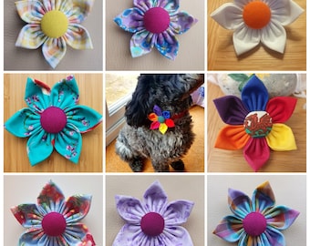 May include: Nine different fabric flower brooches in various colors and patterns. The flowers are all made with a single button in the center and have five petals. The flowers are displayed on a variety of surfaces, including wood, fabric, and a dog's collar.