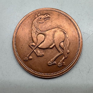 May include: A bronze coin with a detailed relief of a horse in a dynamic pose. The horse is depicted with its head raised and legs extended. The coin's edge has a series of small, raised dots. The coin has a diameter of approximately 3 cm.