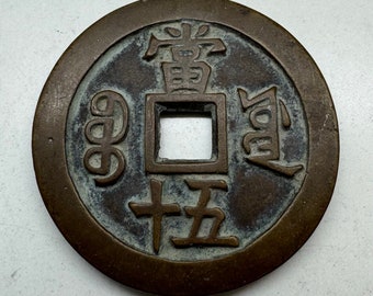 Könnte beinhalten: Eine runde, bronzene Münze mit chinesischen Schriftzeichen und einem quadratischen Loch in der Mitte. Die Schriftzeichen lauten "Qing-Dynastie" und "Zehn Cash".