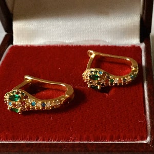 Peut inclure: Une paire de boucles d'oreilles dorées en forme de serpent, serties de diverses pierres précieuses colorées. Les boucles d'oreilles sont présentées dans un écrin en velours rouge. Les pierres précieuses comprennent des pierres vertes, rouges, bleues et blanches.