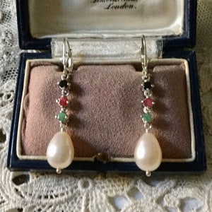 Peut inclure: Une paire de boucles d'oreilles pendantes en argent avec une perle et quatre pierres précieuses. Les pierres précieuses sont noires, rouges et vertes. Les boucles d'oreilles sont dans un écrin en velours bleu avec une étiquette qui indique "A. Wood, 24 Carey St., Lincoln's Inn, London."