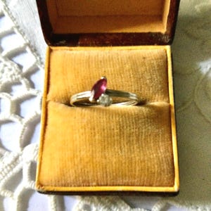 Peut inclure: Bague en argent ornée d'un rubis taille marquise et d'un petit diamant, présentée dans un écrin à bijoux vintage marron avec un intérieur en velours doré. La bague est au centre, mettant en valeur les pierres précieuses.