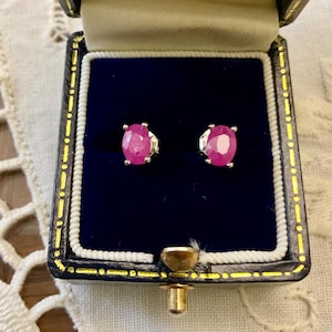 Peut inclure: Une paire de boucles d'oreilles en rubis de forme ovale serties d'argent, présentées dans un écrin à bijoux en velours noir avec un fermoir doré.