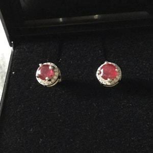 Peut inclure: Une paire de boucles d'oreilles en argent avec une pierre précieuse rouge entourée de petites pierres blanches.