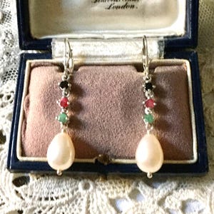 Peut inclure: Paire de boucles d'oreilles pendantes en argent avec une perle nacrée en forme de goutte d'eau. Les boucles d'oreilles comportent une rangée de pierres précieuses noires, rouges et vertes. Présentées dans un écrin bleu avec intérieur rose.