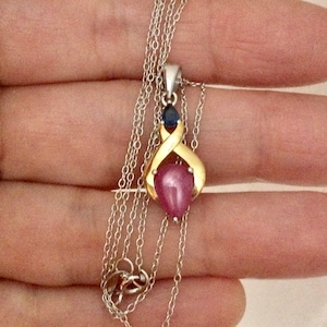 May include: A silver chain necklace with a gold pendant featuring a pink heart-shaped gemstone and two blue gemstones.