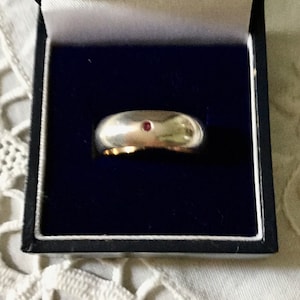 Peut inclure: Une bague en argent avec une petite pierre précieuse rouge sertie au centre.