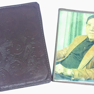 May include: Two brown leather wallets, one with an embossed design and the other with a photo of a man in a brown jacket.