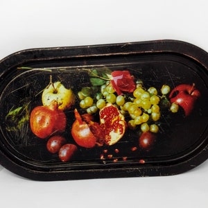 May include: A black oval tray with a painted design of fruit, including pomegranates, grapes, and apples. The tray has a raised rim and a glossy finish.