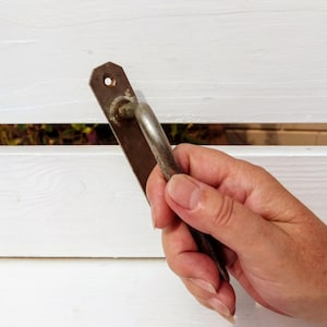 Pode incluir: Uma mão segurando uma maçaneta de porta de metal enferrujada sobre um fundo branco.