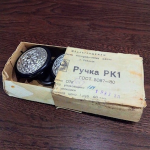 May include: A small cardboard box with a white label that reads "Ручка РК1 ГОСТ 5087-80" and "ничная цена 1 руб. 60 коп." The box contains two black and silver door knobs with a decorative design.