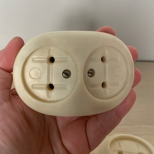 Könnte beinhalten: Zwei weiße Vintage-Steckdosen mit jeweils zwei Stiften. Die Steckdosen sind auf einer weißen Kunststoffbasis montiert.
