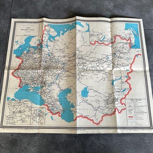 May include: Folded vintage map of the USSR, featuring a detailed geographical layout with blue water bodies and a red border. The map includes text in Russian and is printed on aged paper, showing signs of wear.