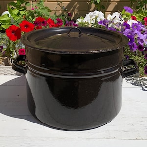 May include: A large, black enamel stock pot with a lid. The pot has two handles on the sides and a single handle on the lid.