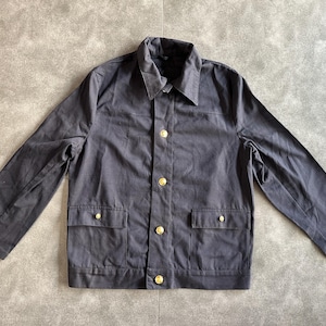 May include: A dark gray jacket with a collared neckline, two front pockets, and gold-colored buttons. The jacket has long sleeves and a classic design, suitable for various occasions. The fabric appears to be a durable material.