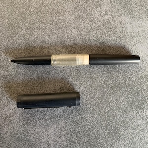 Könnte beinhalten: Ein schwarzer Füllfederhalter mit einer transparenten Tintenpatrone und einer passenden schwarzen Kappe.