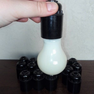 Puede incluir: Primer plano de una bombilla blanca con un casquillo de plástico negro. La bombilla está rodeada de varios casquillos de plástico negro.