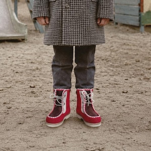 Könnte beinhalten: Ein Paar Stiefeletten mit einem zweifarbigen Design in leuchtendem Rot und Dunkelbraun sowie weißen Ziernähten entlang der Kanten. Die Stiefel verfügen über eine Schnürung mit weißen Schnürsenkeln und eine dicke, helle Sohle für Halt.