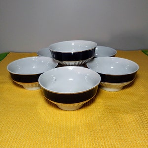 May include: Six white ceramic bowls with a blue and gold trim. The bowls are arranged in a circle on a yellow surface.