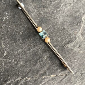 Könnte beinhalten: Silberfarbene Brosche mit einem hellblauen, quadratischen Edelstein und zwei cremefarbenen Perlen. Die Brosche ist lang und schlank, mit einem schlichten, eleganten Design. Wahrscheinlich Vintage oder antik.