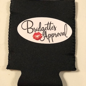 May include: Black neoprene can cooler with a white oval sticker that says "Bridgette's Approval" with a red lip print.