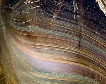 May include: Close-up of a dark brown, iridescent obsidian stone with a layered, striated pattern. The stone has a smooth, polished surface and a slightly curved shape.