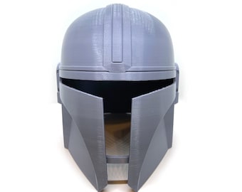 May include: A grey plastic helmet with a visor and a raised ridge on the top. The helmet is designed to resemble a Mandalorian helmet from the Star Wars franchise.