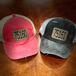 May include: Two distressed trucker hats with mesh back panels. One hat is red with a tan mesh panel and the other is black with a gray mesh panel. Both hats have a brown patch with the number "75160" and "75161" on them.