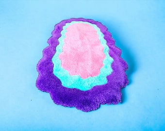 May include: A purple, blue, and pink oval-shaped rug with a wavy edge. The rug is made of soft, fluffy material.