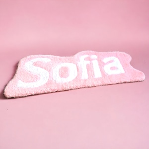 Könnte beinhalten: Eine rosa Badematte mit dem Namen "Sofia" in weißen, flauschigen Buchstaben.