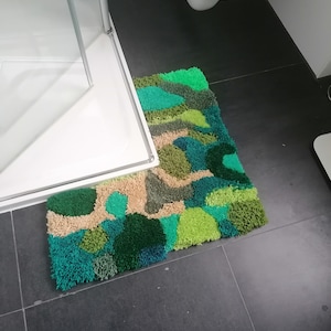 Könnte beinhalten: Eine grüne, blaue und beige Badematte mit einem einzigartigen abstrakten Design. Die Matte besteht aus flauschigem, strukturiertem Garn und ist perfekt, um jedem Badezimmer einen Hauch von Farbe und Stil zu verleihen.