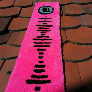 Op de afbeelding: Een roze kleed met een zwart-wit Spotify-logo. Het kleed ligt op een rode betegelde ondergrond.