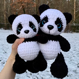 May include: Two handmade crochet panda plush toys made from soft white and black yarn. Each panda features round black ears, a white face with black patches around the eyes, a small black nose, and bright blue glittery eyes with long lashes.